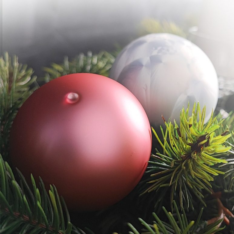 2 Christbaumkugeln aus Glas liegen dekorativ auf Tannenzweige - eine Kugeln in Rosé matt und eine in weiß Icing Design
