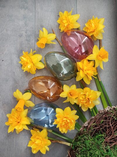 4 Ostereier aus Glas in einem transparenten Design in blau, orange, grün und rot mit Narzissen dekoriert